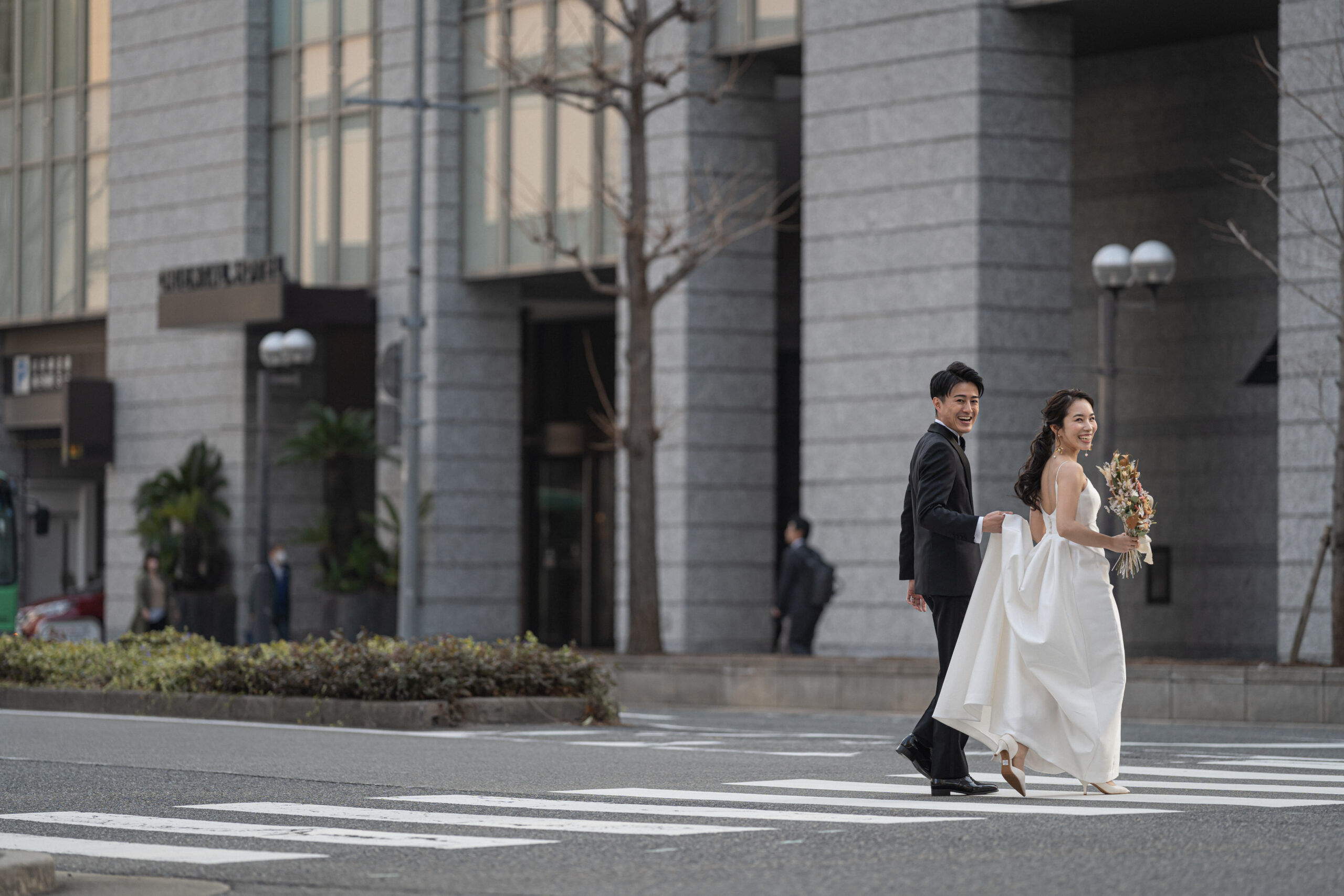 トリートのリラックス感のあるウエディングドレスとブラックタキシードでオリエンタルホテル神戸を背景に居留地の美しい街並みを歩くご新郎様とご新婦様