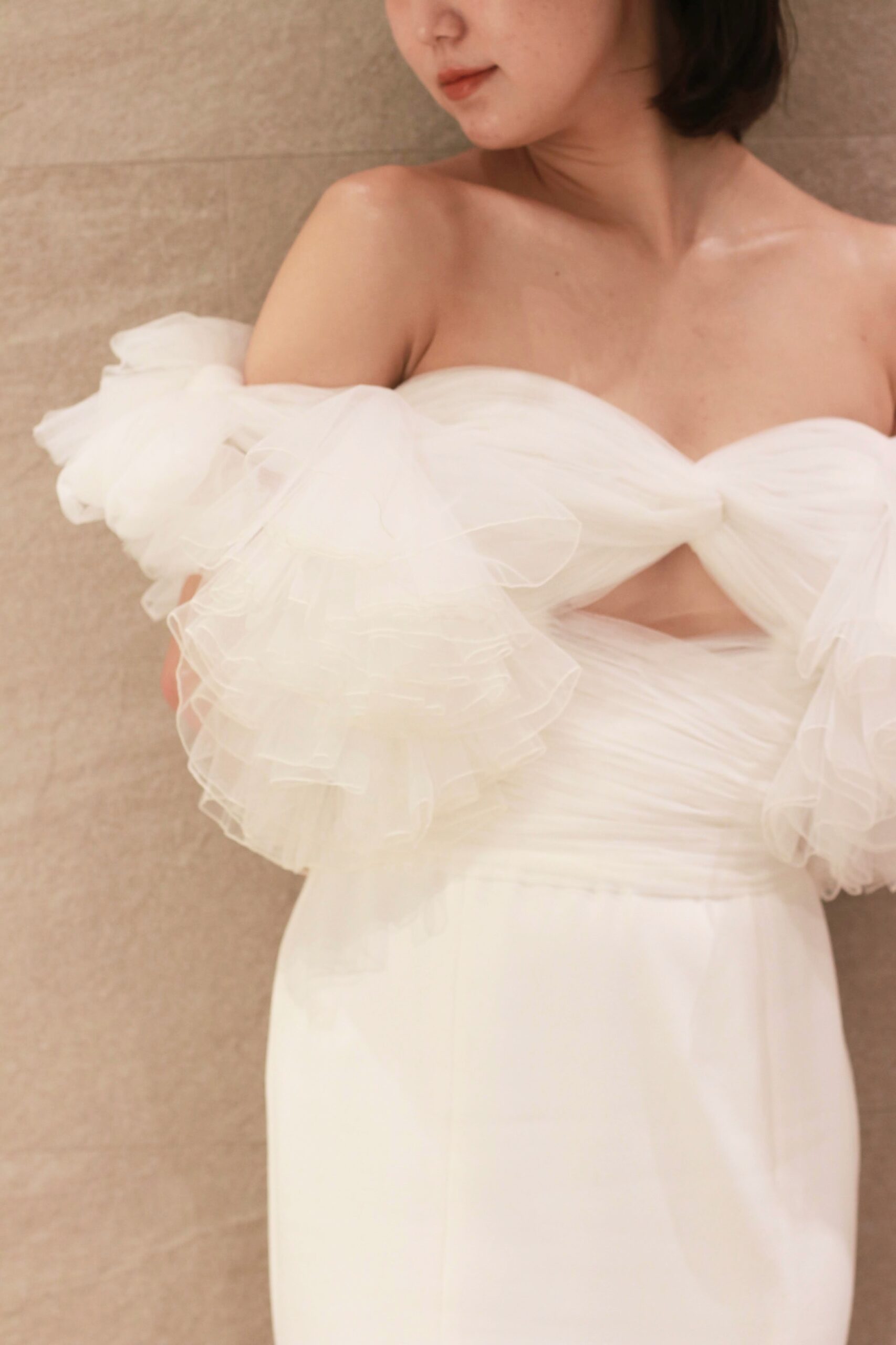 夏の結婚式におすすめのウェディングドレスは、エアリーなチュールのトップスが軽やかで、オフショルダーがデコルテを華奢にみせるスレンダーなデザインです