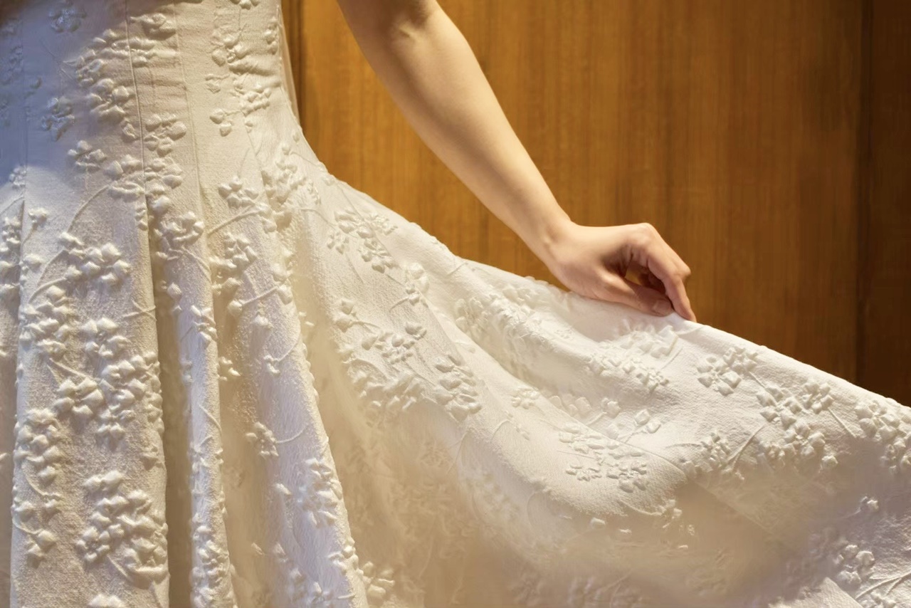 ぷっくりとしたジャガード織りの桜の花のモチーフが華やかなレラ ローズの真っ白なウェディングドレスは、Aラインの広がりがとても綺麗
