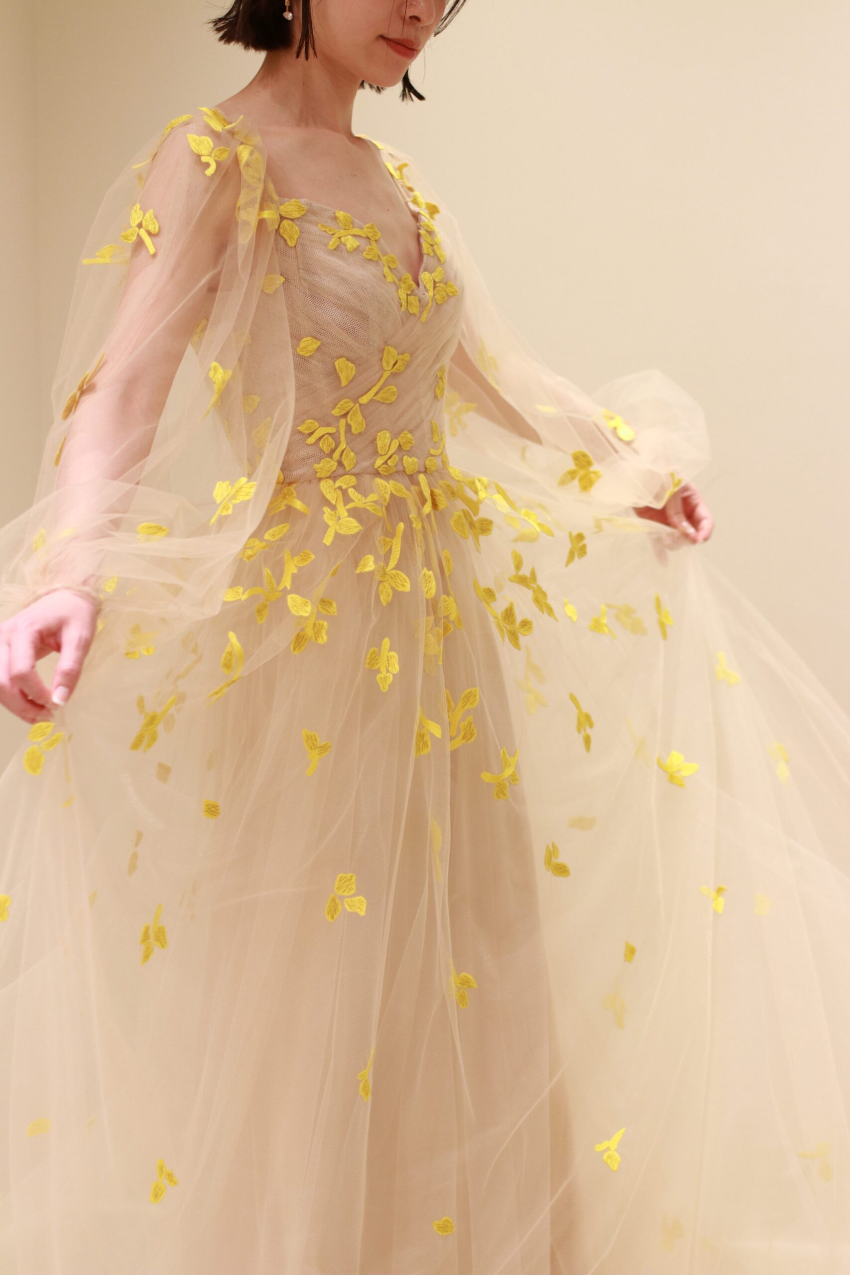 ザトリートドレッシングに入荷したモニークルイリエの新作カラードレスはベージュの柔らかなチュールの上に、イエローの刺繍で花びらの施されたデザインで花嫁の動きに合わせて可憐な印象を演出します。
